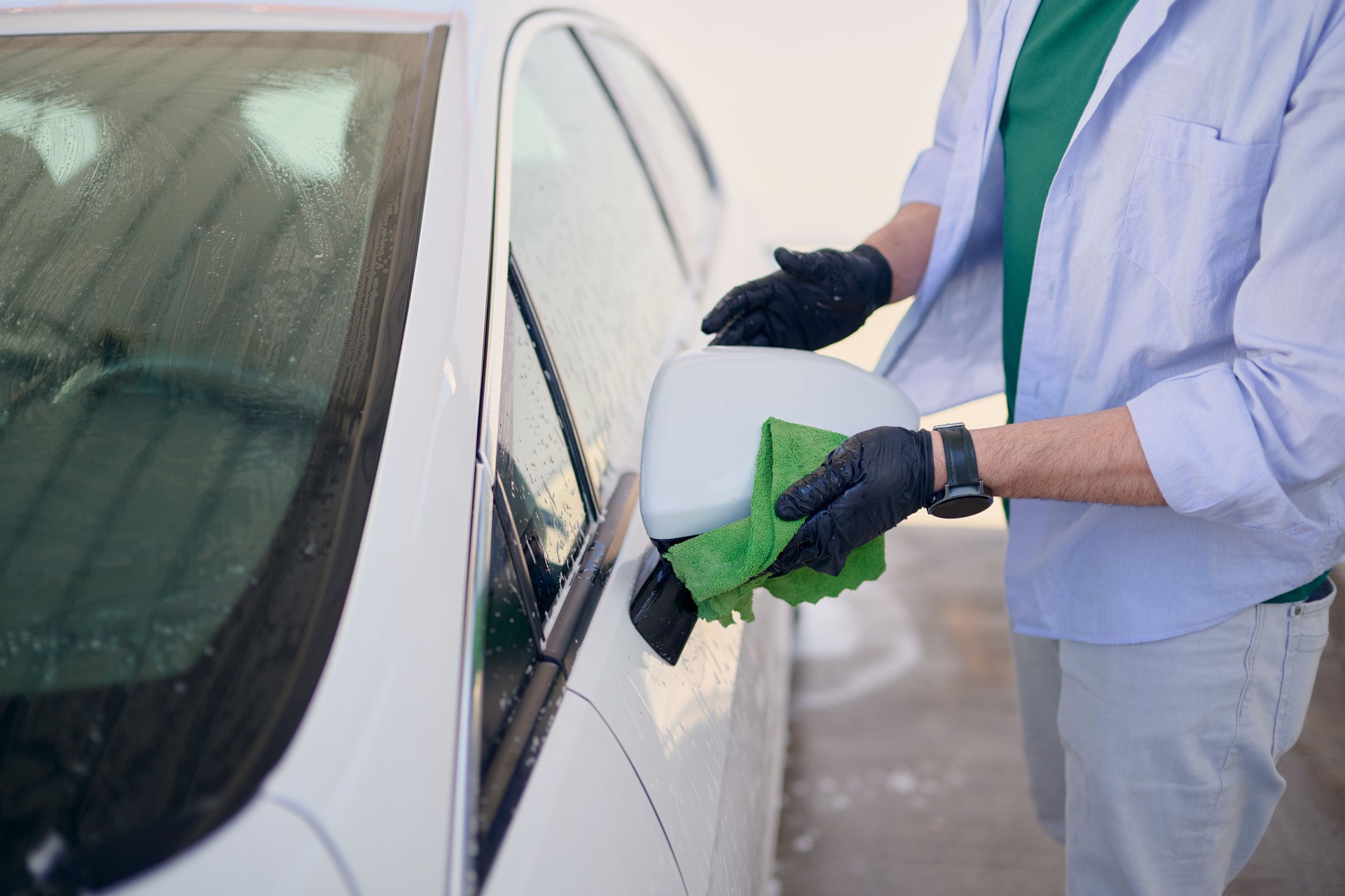 Car wash worker cleaning rearview mirror with microfiber cloth